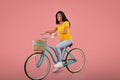 Full length portrait of beautiful African American woman riding vintage bicycle over pink studio background Royalty Free Stock Photo