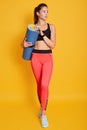 Full length portrait of beautiful athletic young woman holding yoga mat in hands, looking aside, ready for working out, sporty Royalty Free Stock Photo