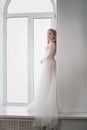 a full-length portrait of a beautiful bride with red hair in a white transparent dress stands in the arch of the window Royalty Free Stock Photo