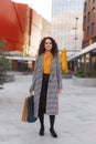 Full length portrait of a beautiful curly young woman with many shopping bags, over buildings background