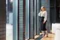 Full length portrait of beautiful elegant businesslady looking out window of business center and talking on cellphone. indoors Royalty Free Stock Photo