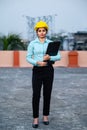 Full length portrait of beautiful female engineer wearing a protective helmet and holding files in hand while looking at camera Royalty Free Stock Photo