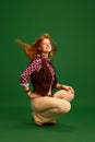 Full length portrait of beautiful red-haired girl, cowgirl sitting and wind blowing her hair against green studio Royalty Free Stock Photo