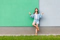 Full length portrait of beautiful woman in casual jeans denim style in summertime standing near green and light blue wall and