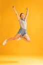 Full-length portrait of beautiful young girl in casual outfit jumping, posing isolated over yellow studio background Royalty Free Stock Photo