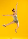 Full-length portrait of beautiful young girl posing, cheerfully jumping isolated over yellow studio background. Having Royalty Free Stock Photo