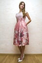 Full length portrait of a beautiful young happy confident girl with long blond hair posing in summer dress with pink floral design Royalty Free Stock Photo