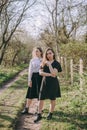 Full length portrait beautiful young sisters in the green spring garden, hugging in the field in the sunshine. Having fun together