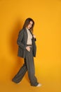 Full length portrait of beautiful young woman in fashionable suit on yellow background. Business attire Royalty Free Stock Photo