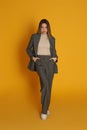 Full length portrait of beautiful young woman in fashionable suit on yellow background. Business attire Royalty Free Stock Photo