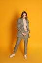 Full length portrait of beautiful young woman in fashionable suit on yellow background. Business attire Royalty Free Stock Photo