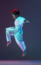 Full-length portrait of boy, karateka in white kimono, jumping, training isolated over gradient blue background in neon Royalty Free Stock Photo