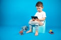 Full-length portrait boy with smartphone sitting on the pot on isolated blue. Royalty Free Stock Photo