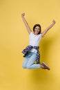 Full-length portrait of carefree girl in white shirt and jean jumping on yellow background. Royalty Free Stock Photo