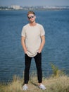 Stylish young man in sunglasses. Tall, cool guy walking near the river on a blurred background. College style concept.