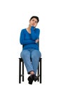 Full length portrait of casual young woman seated on a chair keeps hand under chin looking up thoughtful isolated over white