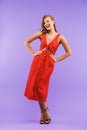 Full length portrait of caucasian cute woman 20s wearing red dress smiling at camera, standing isolated over violet background Royalty Free Stock Photo