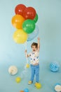 Full length portrait of cheerful boy holding balons posing against blue background