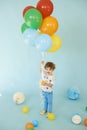 Full length portrait of cheerful boy holding balons posing against blue background