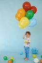 Full length portrait of cheerful boy holding balons posing against blue background