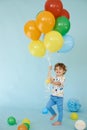 Full length portrait of cheerful boy holding balons posing against blue background