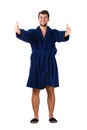 Full length portrait of cheerful young man, positive smiling showing thumbs up gesture, wears blue bathrobe, isolated over white Royalty Free Stock Photo