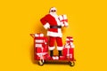 Full length portrait of confident aged santa stand pushcart pile stack festive christmas giftbox isolated on yellow