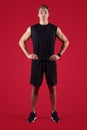 Full length portrait of determined male fitness model looking at camera on red studio background