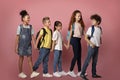 Full length portrait of diverse schoolkids holding hands and walking over pink background