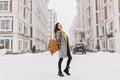 Full-length portrait of european girl wears elegant coat in snowy weather. Cheerful young woman with stylish backpack