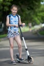 Full-length portrait of European preteen girl standing near scooter on an asphalt road Royalty Free Stock Photo