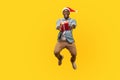 Full length portrait of extremely happy young man in santa hat and casual denim shirt jumping or flying and giving christmas gift Royalty Free Stock Photo