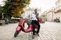 Full length portrait of fashionable African businessman wearing black pants and white shirt, leaning on red scooter in Royalty Free Stock Photo