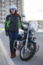 Full length portrait of female motorcyclist in safety outfit standing near classic bike on urban road
