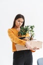 Full length portrait of frustrated young woman dressed in elegant wear holding box with office supplies due to firing