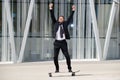 Full length fun businessman standing on skateboard with arms raised