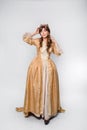 A full-length portrait of a girl in a golden rococo gown with a crown on his head posing isolated on a white background