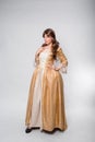 A full-length portrait of a girl in a golden rococo gown posing isolated on a white background
