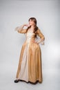 A full-length portrait of a girl in a golden rococo gown posing isolated on a white background