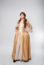 A full-length portrait of a girl in a golden rococo gown posing isolated on a white background