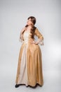 A full-length portrait of a girl in a golden rococo gown posing isolated on a white background