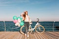 Full-length portrait of gorgeous female bicyclist standing on the pier on sea background in her birthday. Charming