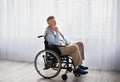 Full length portrait of handicapped senior man in wheelchair feeling desperate and lonely, looking out window indoors Royalty Free Stock Photo