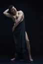 Full-length portrait of handsome man with relief, muscular, shirtless body posing in dark fabric against black studio Royalty Free Stock Photo