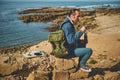 Full length portrait of a handsome hiker traveler man sitting on a rock by sea, drinking hot drink. People Travel Nature Royalty Free Stock Photo