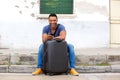 Full length handsome young african man sitting with suitcase and smart phone Royalty Free Stock Photo