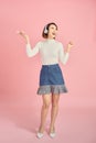 Full length portrait of a happy asian businesswoman listening to music with headphones while dancing isolated over pink background Royalty Free Stock Photo