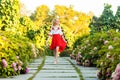 Full length portrait of happy barefoot attractive woman in stylish red white dress holding shoes and walking on tile path in