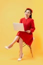Full length portrait of a happy casual asian woman holding laptop computer while sitting on a chair over orange background Royalty Free Stock Photo