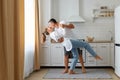 Full length portrait of happy couple wearing casual clothing dancing together in kitchen, husband kissing his wife, being happy to Royalty Free Stock Photo